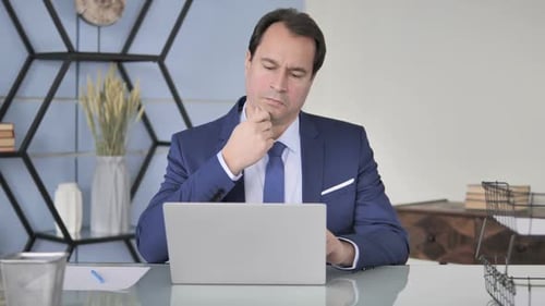Man in Suit Thinking at Desk With Laptop