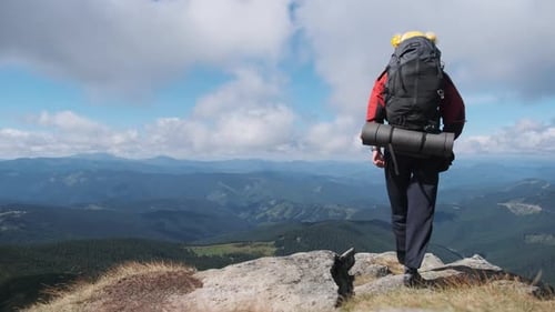 Tourist with Backpack on the Top of Mountain Near the Cliff Raises Hands To Side