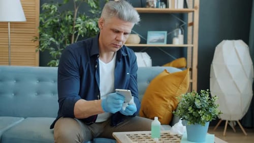 Man Cleans Smartphone with Wipe Wearing Gloves