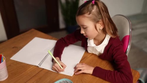 Écolière concentrée assise au bureau en train de faire ses devoirs d'écriture