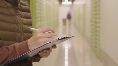 Woman Writes on Clipboard in Office Corridor