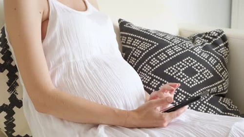 Pregnant Woman Using Phone Sitting on White Couch
