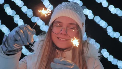 Sparklers in the Hands of a Girl in Mittens Against the Background of the City's Christmas Lights