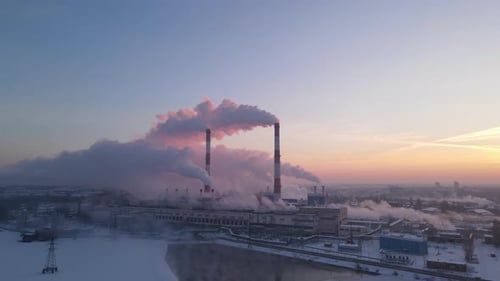 Smokestacks of factory smoke over sunrise sky background at freezing weather morning with haze