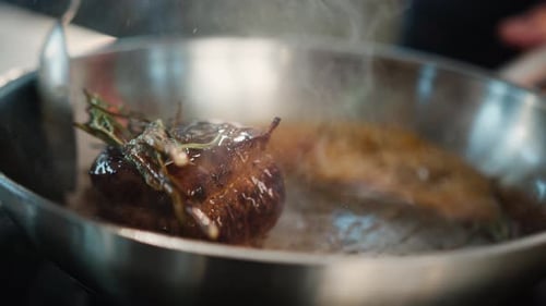 Close-up of filet mignon with thyme being cooked in a frying pan