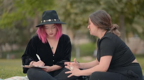 Fille aux cheveux roses prend des notes dans le bloc-notes pendant que son amie lui dicte