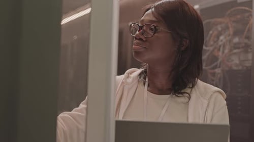 Focused Woman Working in Server Room on Laptop