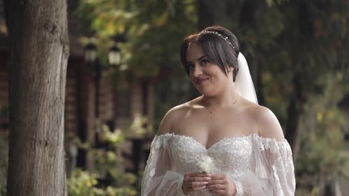 Beautiful Stylish Bride in White Wedding Dress and Veil Holding Wedding Bouquet in Hands in Park