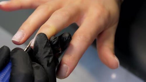 Kosmetikerin in Handschuhen entfernt Nagelhaut von Frauennägeln