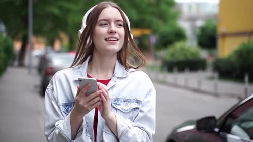 Girl listening to music with headphones and smartphone, walking on the street
