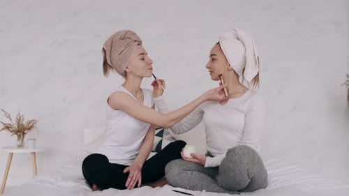 Two Women Applying Makeup to Each Other on Bed