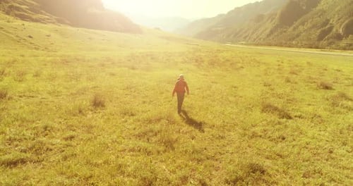 Flight Over Backpack Hiking Tourist Walking Across Green Mountain Field. Huge Rural Valley at Summer