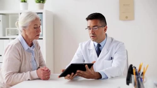 Doctor Consults with Senior Woman Using Tablet in Office