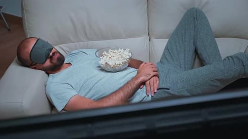 Man Sleeping on Couch with Popcorn and Mask