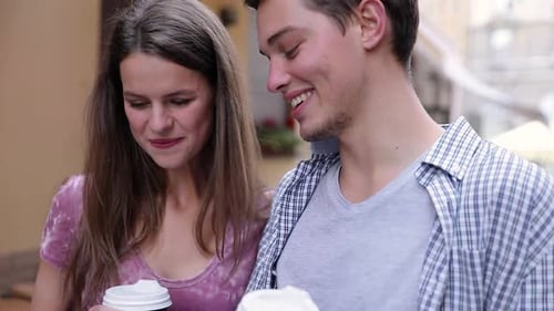 Glückliches Paar benutzt Handy und trinkt Kaffee im Freien
