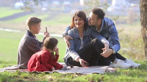 Happy family resting together on green grass in city park.