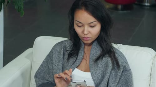 Woman Using Smartphone on White Sofa Indoors