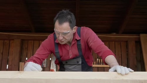 Worker in Goggles Makes Notes with Carpenters Pencil on a Wooden Blank