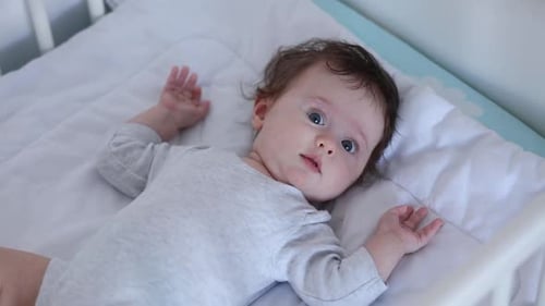 Cute Infant Lying in Crib on White Blanket
