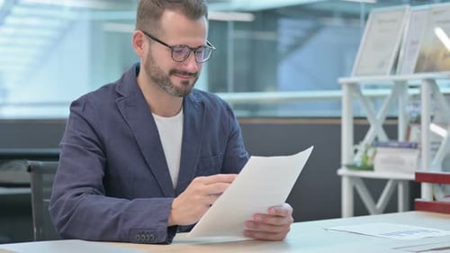 Middle Aged Businessman Celebrating While Reading Documents in Office