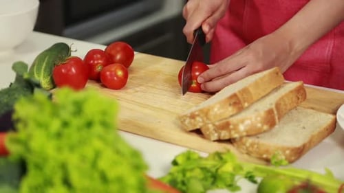 close up of female hand cutting tomato on board in kitchen room