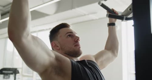 Junger Muskelsportler trainiert in einem modernen Fitnessstudio und macht Klimmzüge