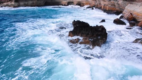 Sea Washes the Rocky Shore Above Aerial Shot Flying Over Coastline Cliffside with Blue Pure Water