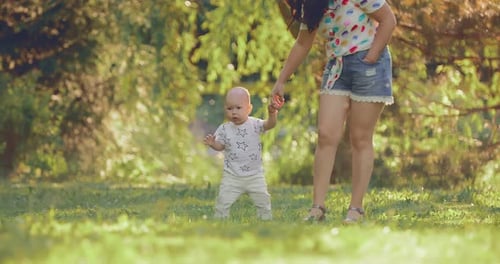 Pretty Baby Is Standing on a Green Lawn, a Summer Walk in the Park. Little Son Holds His Mother