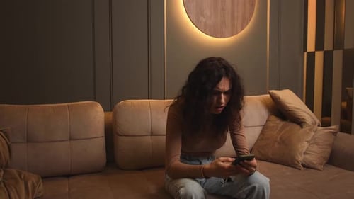 Young Woman Reading on Cell Phone, Sitting on Couch