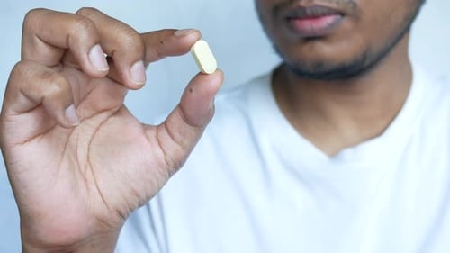 Person Holding Small Pill Close Up