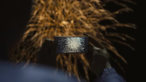 Person Filming Fireworks with Smartphone at Night