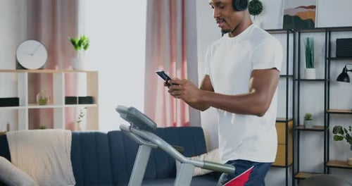 Man Using Phone on Treadmill with Headphones