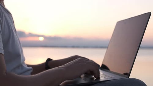 Close up of male hands typing on laptop at the shore. Digital nomad or remote worker concept