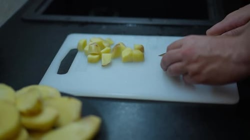 Side View Male Caucasian Hands Slicing Potato on Cutting Board with Kitchen Knife