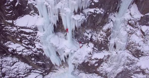 Aerial drone view of a man ice climbing on a frozen waterfall in the mountains.
