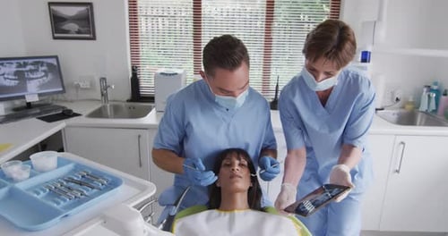 Caucasian male dentist with face mask examining teeth of female patient at modern dental clinic