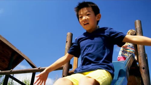 Happy schoolboy playing on slide in playground