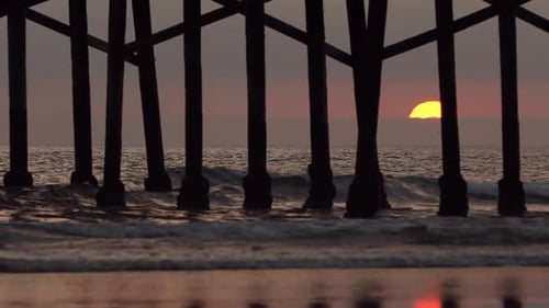 Sun setting behind pier viewing waves in the ocean