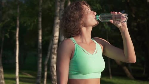 Woman Drinking Water After Fitness Workout in Park
