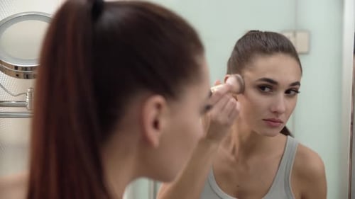 Woman Applying Makeup with Brush in Bathroom Mirror