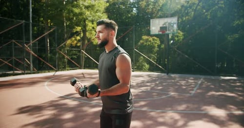 Sporty Man Lifting Weights with Both Hands in a Public Park Dumbbell Training