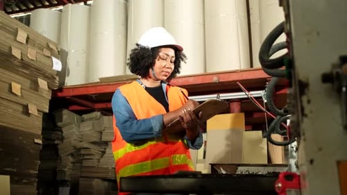 A female industrial worker checks the machine in a paper manufacturing factory.