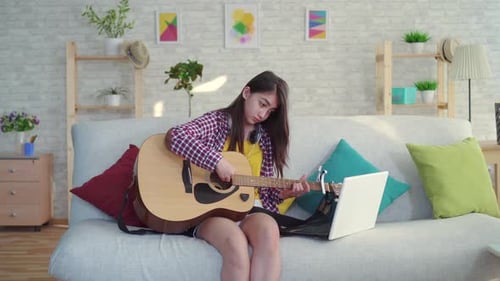 Teen Girl Plays Guitar at Home with Laptop