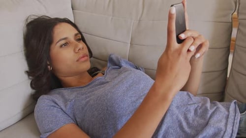 Woman Lying on Couch Using Smartphone Indoors
