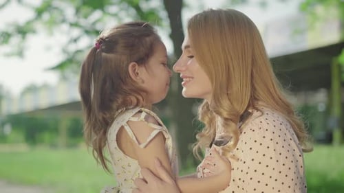 Side View Close-up of Smiling Young Blond Mother and Brunette Little Daughter Hugging and Talking in