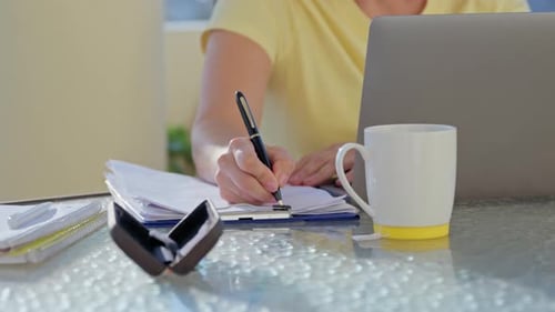 Woman Writes on Notepad While Using Laptop