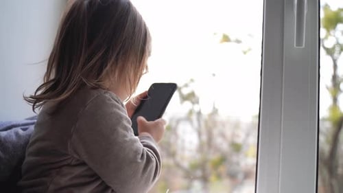 Child Using Mobile Phone Near Window