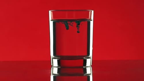 Two Drops on Black Ink Dripping Into Clear Water in Glass Standing on Red Background in Slowmotion