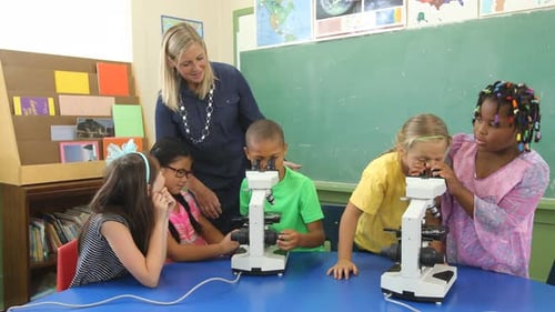 Teacher and students look through microscopes in school classroom