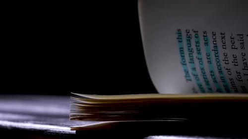 A Beam of Light Falls on the Book Which Lies on the Table in a Studio on a Black Background